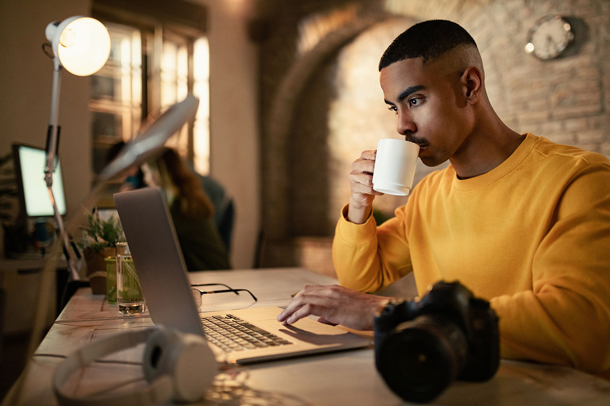 Young black businessman drinking coffee while working late on a computer in the office.